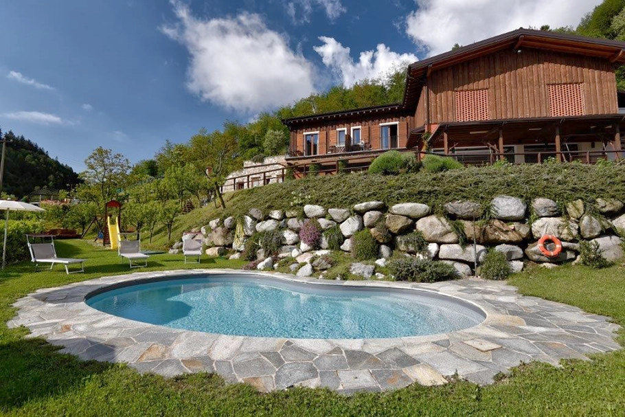 Wooden farmhouse with swimming pool surrounded by greenery, between hills and nature